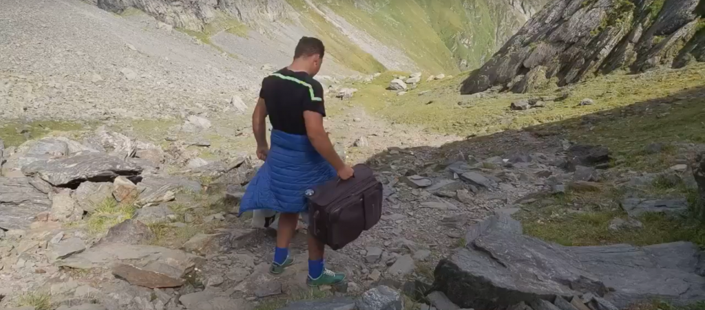VIDEO Un bărbat merge pe jos, de la Bâlea Lac la Moldoveanu, cu trolerul în mână, acompaniat de o boxă cu muzică populară