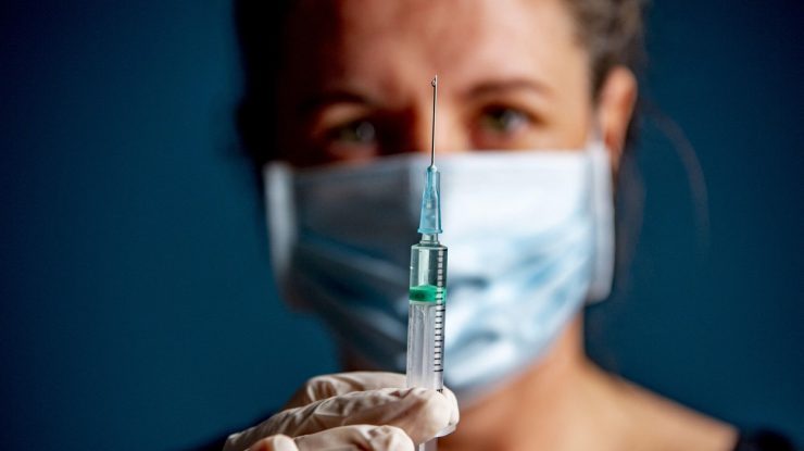 o femeie cu masca tine in dreptul fetei o seringa.