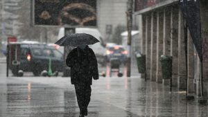 Bărbat care merge pe stradă și ține o umbrelă în mână.