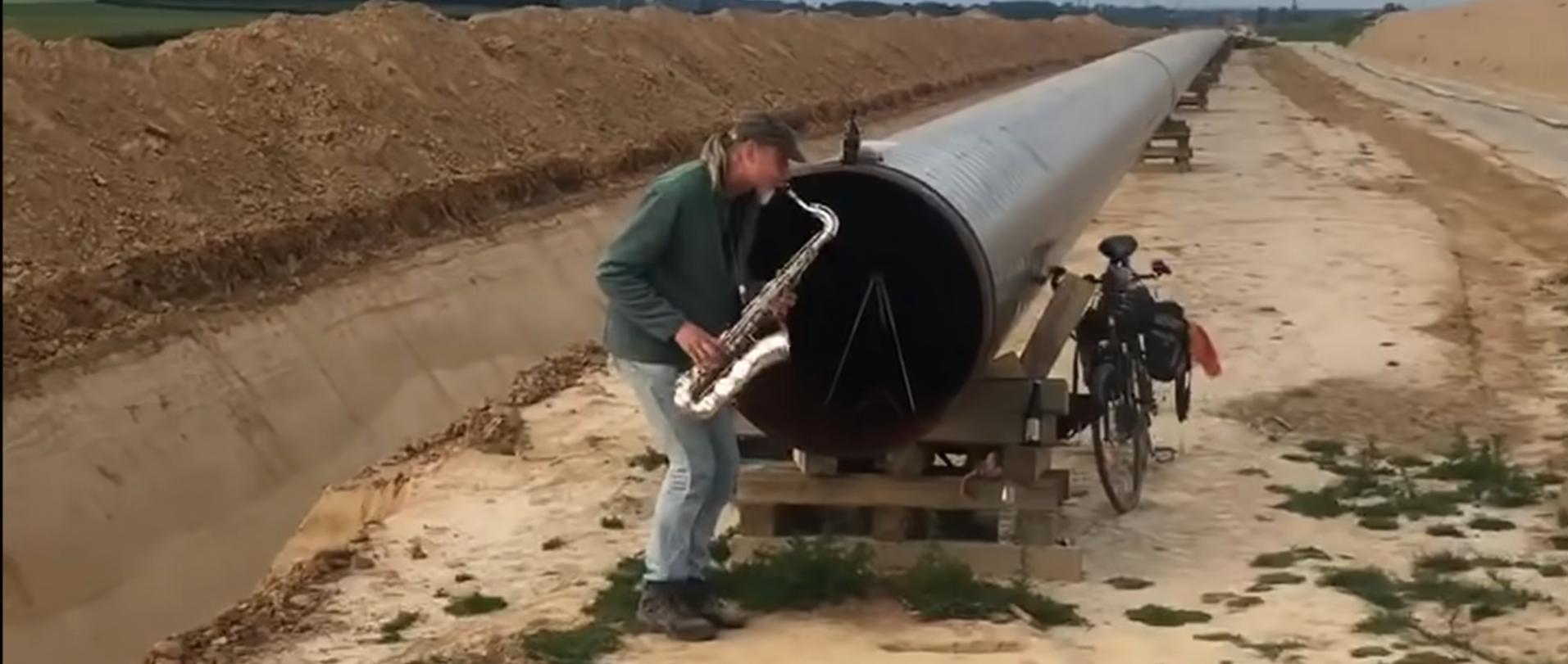 Un german cântă la saxofon în fața unui gazoduct, în pustietate. Pare că are o întreagă orchestră