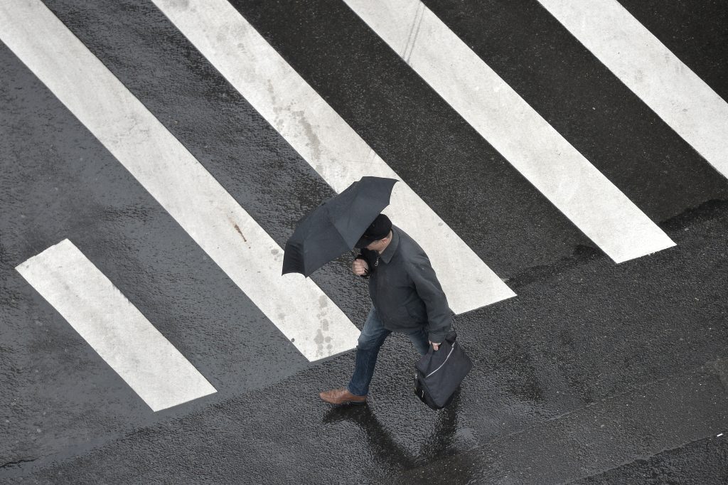 Un bărbat care traversează strada în timp ce ține o umbrelă.