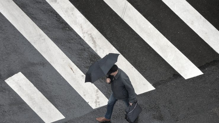 Un bărbat care traversează strada în timp ce ține o umbrelă.
