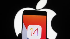 In this photo illustration the iOS 14 logo of the iOS mobile operating system is seen displayed on a mobile phone with an Apple logo in the background.