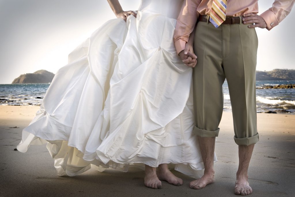 Bărbat și femeie ținându-se de mână. Femeia este îmbrăcată în rochie de mireasă.