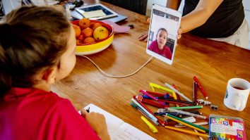 Copil care participă la școala online și are pe masă creioane și caiete.