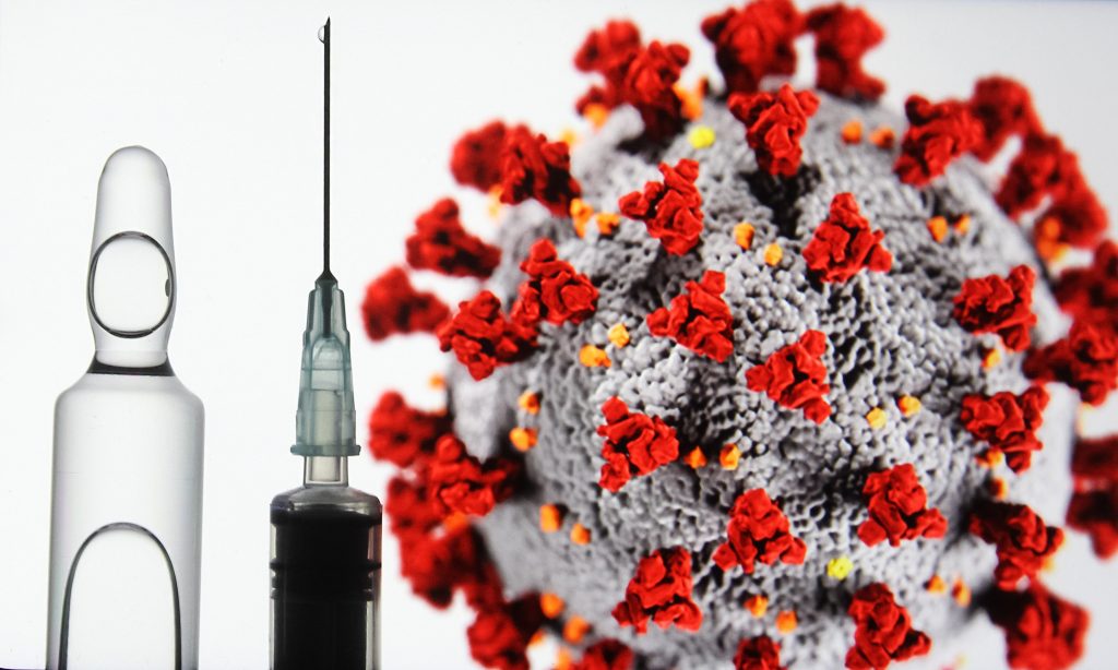 Coronavirusul stă lângă o fiolă de vaccin și lângă o seringă.