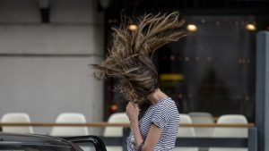 O tânără își apără fața de vânt în timp ce părul îi este suflat de rafală, în București.