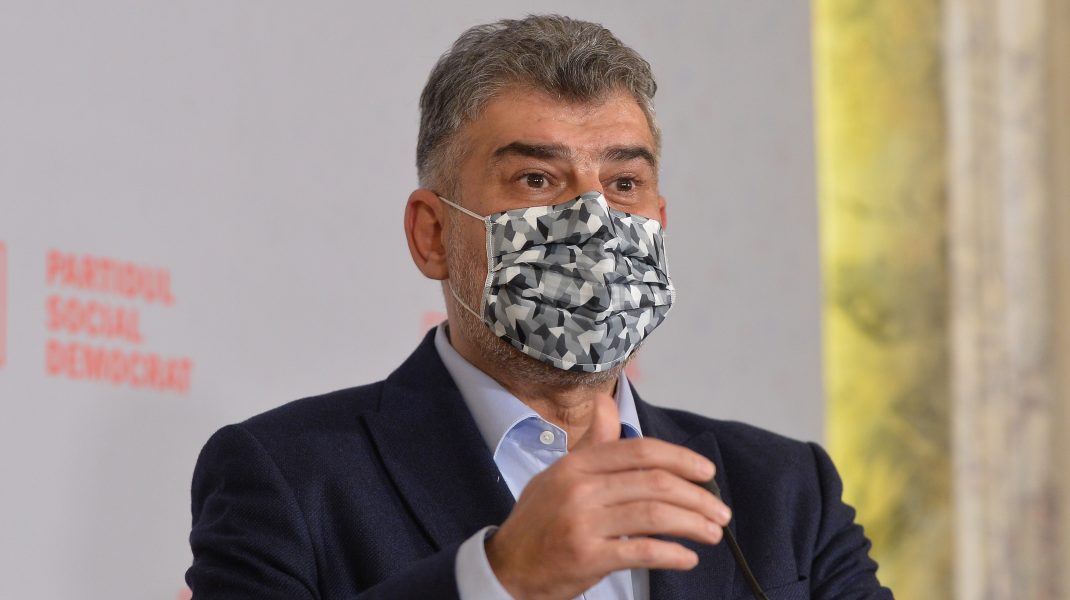 Marcel Ciolacu poartă mască de protecție în timp ce vorbește la microfon.