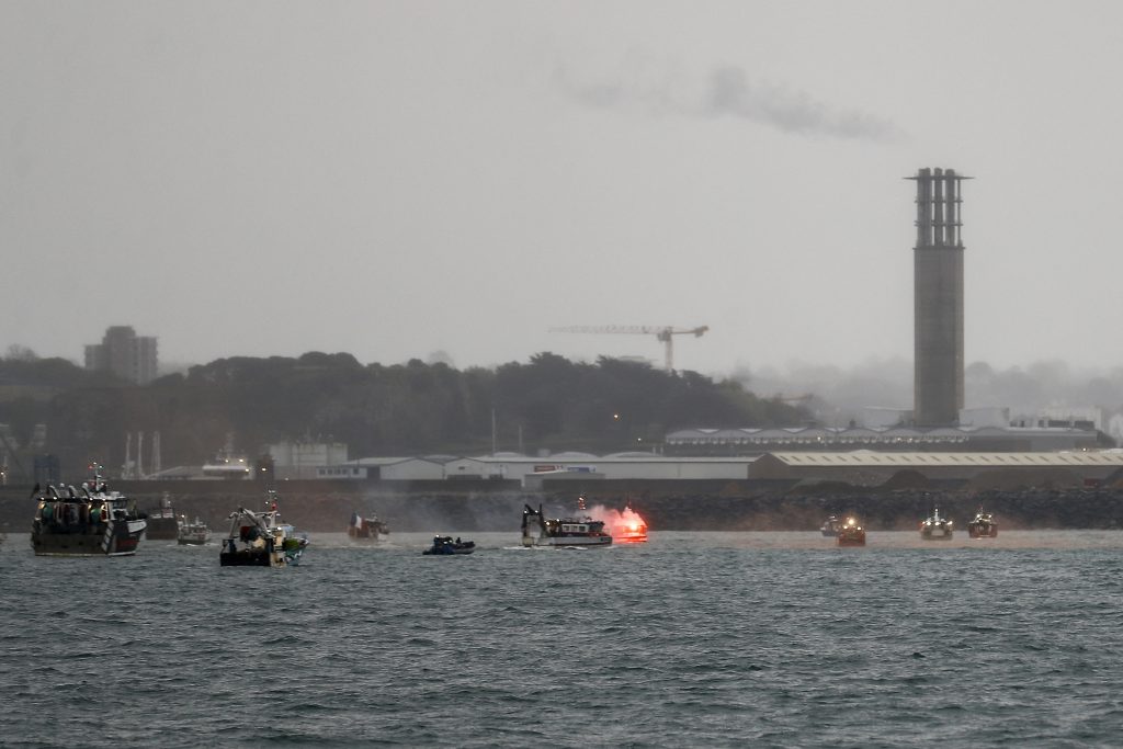 O rachetă de semnalizare este aprinsă în timp ce bărci de pescuit franceze protestează în fața portului Saint Helier, în largul insulei britanice Jersey.