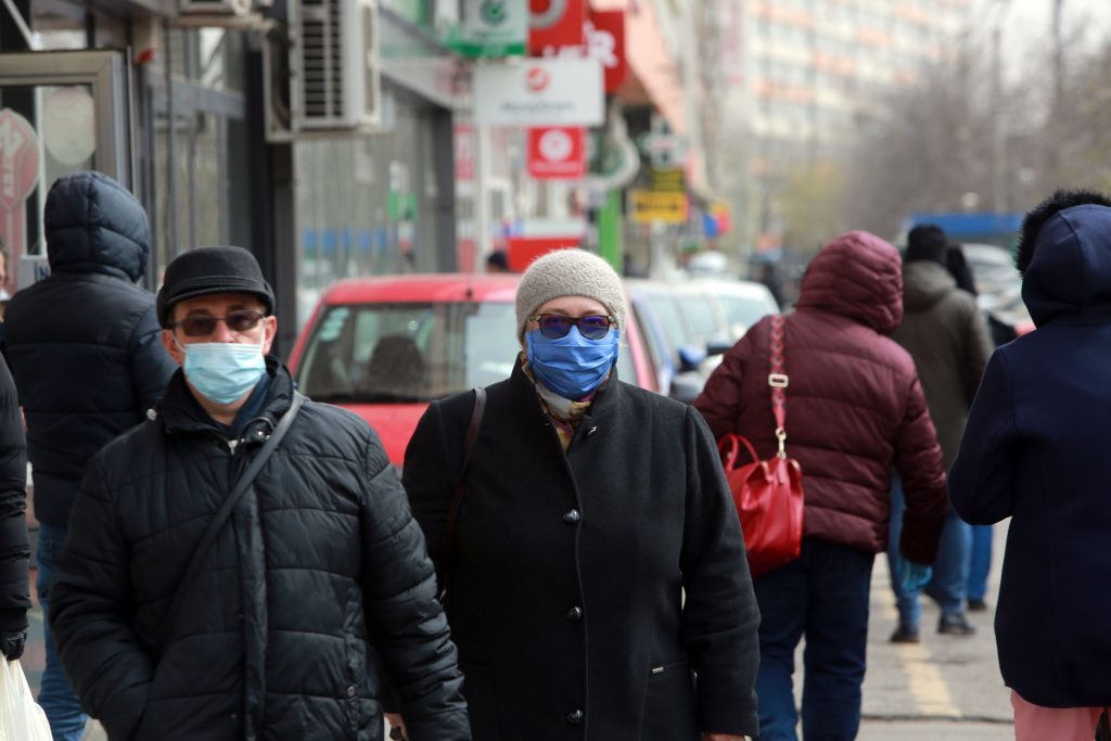 Oameni bătrâni care se plimbă pe străzile din București și poartă mască de protecție.