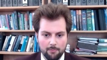 Ștefan Dascălu stă în fața unei biblioteci, la birou, într-un videocall.