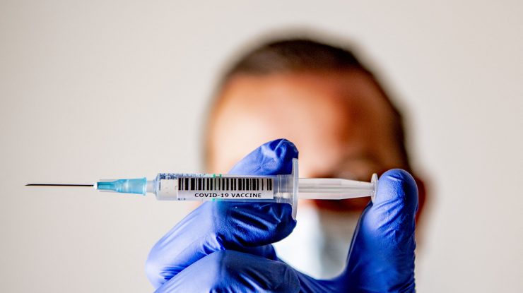 Medic care ține între degete o seringă cu ser anti-COVID.