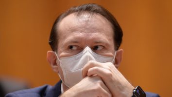 Florin Cîțu se uită pe sub sprâncene în timp ce își pune mâinile pe față.