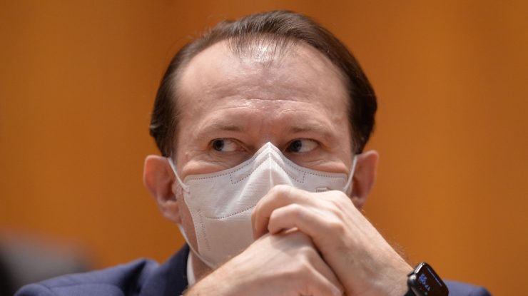 Florin Cîțu se uită pe sub sprâncene în timp ce își pune mâinile pe față.