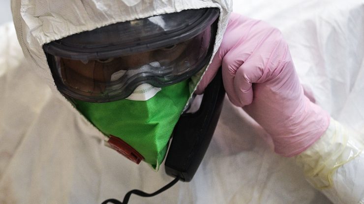 Medic în costum de protecție anti-COVID care vorbește la telefon printr-o mască.