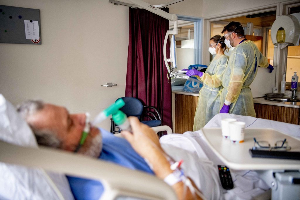 Pacient infectat cu COVID-19 într-un salon de spital, alături de doi doctori.