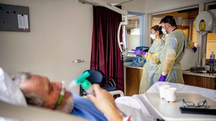 Pacient infectat cu COVID-19 într-un salon de spital, alături de doi doctori.