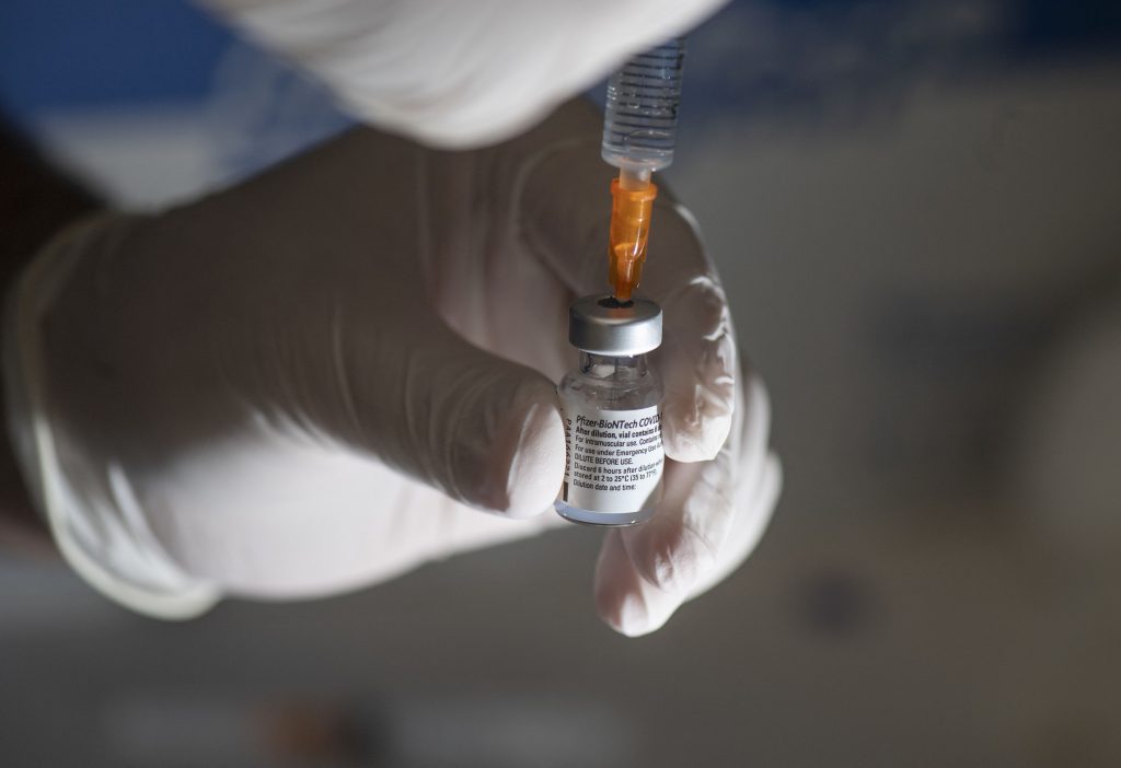 Medic care extrage ser cu o seringă dintr-o doză de vaccin anti-COVID Pfizer.
