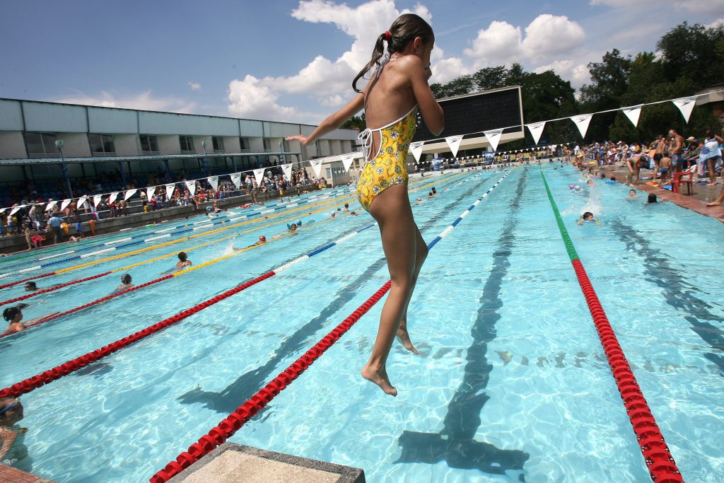 o fetita sare in piscina la un concurs de natatie in aer liber.