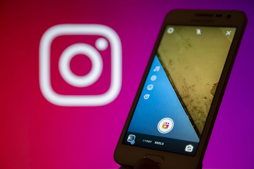 Logo-ul de la Instagram lângă un telefon în care este deschisă aplicația pentru fotografii.