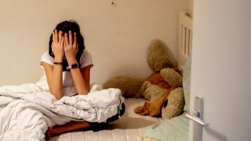 Copil care stă în dormitor, în pat, cu mâinile la ochi.