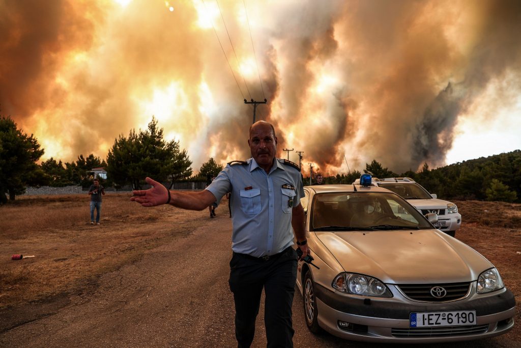 05 august 2021, Grecia, Atena: Un ofițer de poliție lucrează pentru a evacua zona din apropierea unui incendiu de vegetație care arde zona Drossopigi, Varybobi, o suburbie din nord-estul Atenei.