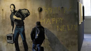 A visitor watches inside an hole of "Steve Jobs", a reproduction of a mural by British artist Banksy, during the unveiling of the "The World of Banksy, The Immersive Experience" exhibition, in Milan, Italy, Thursday, Dec. 2, 2021. An exhibition of 130 works by British street artist Banksy opens Friday in a gallery space inside Milan's Central train Station. The exhibition unveiled on Thursday includes 30 never before seen works by Bansky and highlights pieces by young unknown artists from all over Europe. (AP Photo/Luca Bruno)