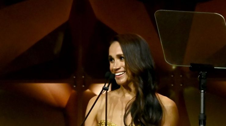 FOTO. Meghan Markle strălucește într-o rochie aurie fără bretele, însoțită de Prințul Harry și mama sa