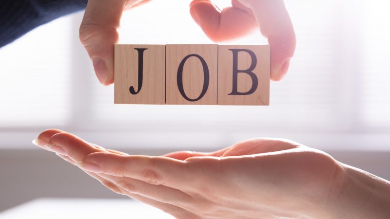 Person Giving Wooden Block With Job Text To Candidate