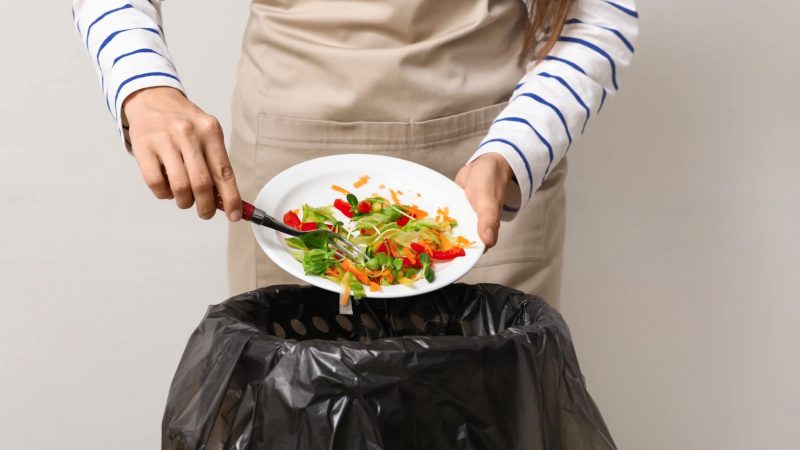 Young,Woman,Throwing,Organic,Food,Into,Trash,Bin,On,Grey